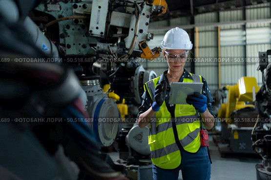 A female engineer installs a program on a robotics arm in a robot warehouse. And test the operation before sending the machine to the customer. Стоковое фото, агентство Ingram Publishing / Фотобанк Лори