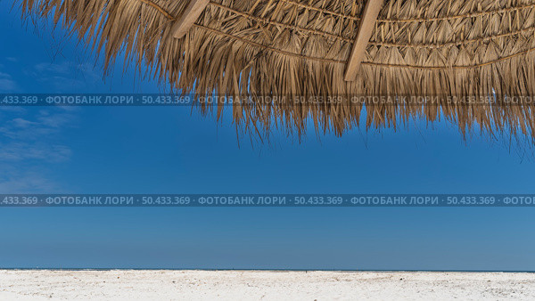 A fragment of a straw sun umbrella against a clear blue sky. Close-up. The upper part of the screen. The crossbars and the weave are visible. At the bottom of the frame is a white sandy beach. Madagascar. Стоковое фото, фотограф Вера Ивановна Кубарева / Фотобанк Лори