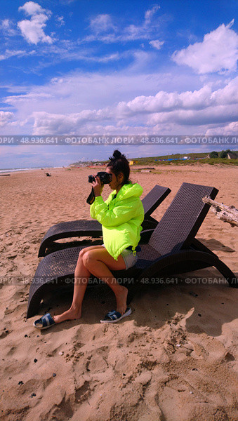 A girl takes pictures of the sea sitting on a chaise longue on the beach on a cool day. Стоковое фото, фотограф K. / Фотобанк Лори