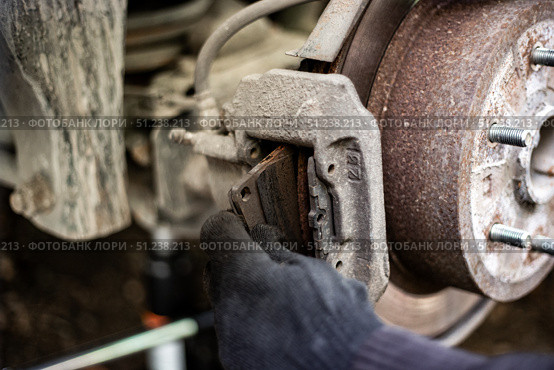 A gloved hand removes a worn brake pad from a car caliper, preparing to replace it. Стоковое фото, фотограф Коханова Наталья / Фотобанк Лори