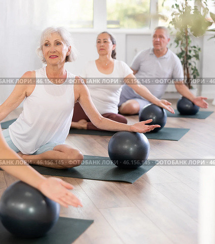 A group of elderly amateurs with a girl instructor perform Eka Pada Rajakapotasana with a soft ball. Стоковое фото, фотограф Яков Филимонов / Фотобанк Лори