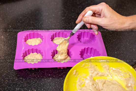 A hand carefully spoons batter into a silicone baking pan, preparing individual servings of banana muffins. Стоковое фото, фотограф Коханова Наталья / Фотобанк Лори