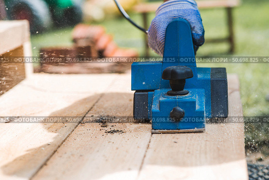 A hand-held electric planer in the hands of a craftsman. A man planing boards with an electric tool. Production of wooden products. Construction, wood processing. Стоковое фото, фотограф Photojuli / Фотобанк Лори
