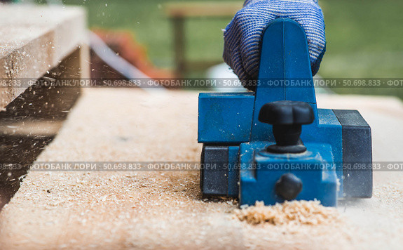 A hand-held electric planer in the hands of a craftsman. A man planing boards with an electric tool. Production of wooden products. Construction, wood processing. Стоковое фото, фотограф Photojuli / Фотобанк Лори