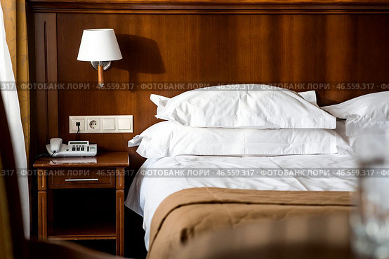 A hotel-type bed with white sheets, pillows and a bedside table in a hotel room or home bedroom. Space for the text. Enjoying the morning concept. Стоковое фото, фотограф Photojuli / Фотобанк Лори
