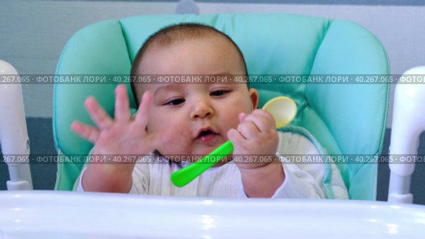 A hungry baby is gnawing on a plastic spoon at the table on a high chair. Teething, whims, itchy gums, introduction of complementary foods. Стоковое видео, видеограф Ольга Симонова / Фотобанк Лори