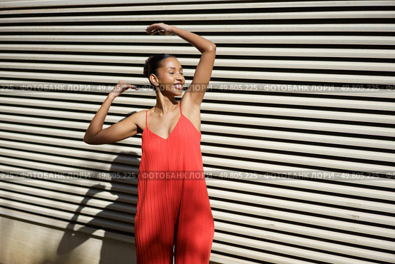A joyful young woman dances in a vibrant red outfit against a colorful backdrop, radiating happiness, confidence, and zest for life, making the moment captivating and unforgettable. A Joyful Dance Painted in Bright Red Outfit, Set Against an EyeCatching Striped Background. Стоковое фото, агентство Ingram Publishing / Фотобанк Лори
