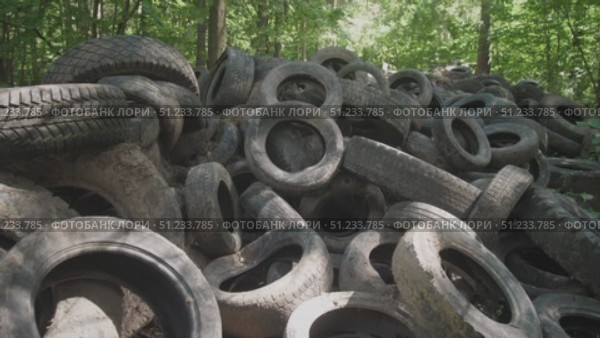 A large collection of old tires accumulates in a wooded area, highlighting the problem of illegal dumping and the persistent issue of waste management in nature. Стоковое видео, видеограф Громов Александр / Фотобанк Лори