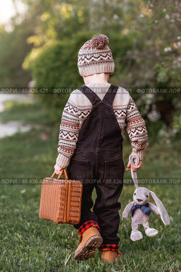 A little boy of 4 years old outdoors with a suitcase and a stuffed rabbit goes on a journey. A beautiful portrait of a child playing on the street. Стоковое фото, фотограф Photojuli / Фотобанк Лори