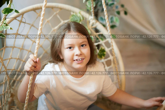 A little girl is relaxing in room with a wicker chair. A schoolgirl is lazy after school. Teen idling at home. Стоковое фото, фотограф Кривошеина Елена Леонидовна / Фотобанк Лори