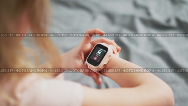 A little girl wears a smartwatch on her wrist and controls the functions by tapping on the screen. Стоковое видео, видеограф Енваев Андрей / Фотобанк Лори
