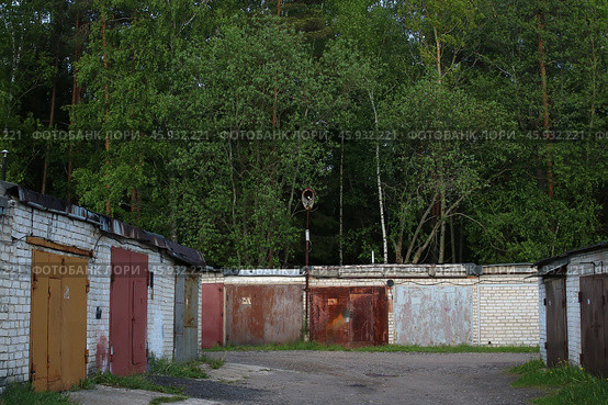 A long row of garages is situated with trees in the background. Стоковое фото, фотограф Аксенова Вера / Фотобанк Лори