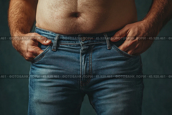 A male figure captured from the chest to the hips. The man is wearing classic blue jeans that fit his figure slightly. The man's hands are in the pockets of the jeans, which gives him a relaxed pose. In the foreground, a small belly is visible, which emphasizes the fullness of the body. The background is muted, dark green, which draws attention to the figure. The image is made with an emphasis on the texture of the fabric and skin, conveying warmth and naturalness. Стоковое AI-изображение, AI-художник Анна Кривицкая / Фотобанк Лори