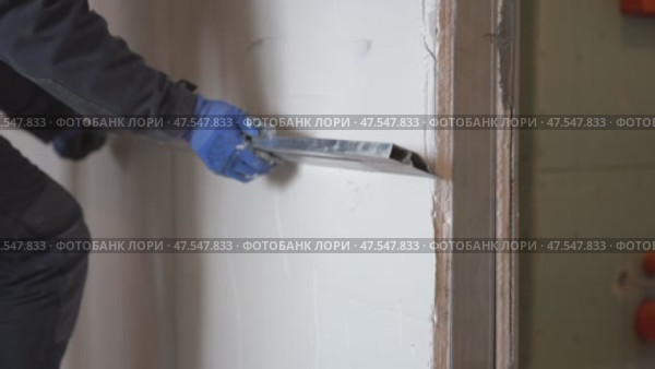 A male plasterer holds a metal ruler called a rule in his hands and aligns a newly plastered wall. Стоковое видео, видеограф Darya Komarova / Фотобанк Лори