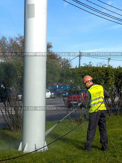 A man in a yellow vest is cleaning a pole with a hose. Russia. Moscow. 05.09.25. Редакционное фото, фотограф Ярославский Максим / Фотобанк Лори