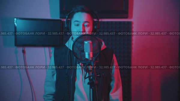 A man in hoodie rapping in the record studio gesticulates while recording his track. Стоковое видео, видеограф Константин Шишкин / Фотобанк Лори