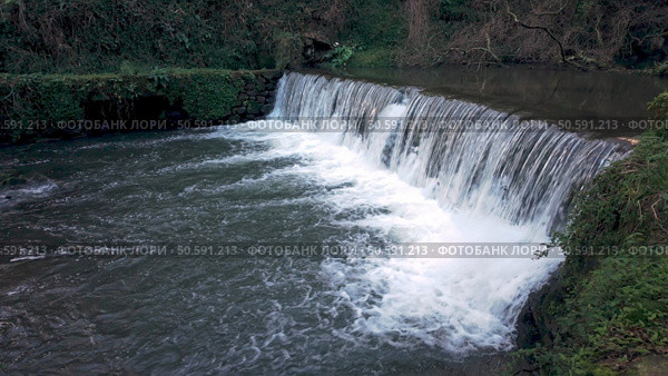 A man-made weir creates a powerful cascade on the river near Cascata do Outeiro. The rushing water and surrounding greenery create a dynamic scene in Oliveira de Azemeis. Стоковое фото, агентство Ingram Publishing / Фотобанк Лори
