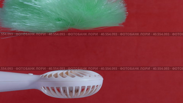 A man presses the power button on a portable portable fan. Shows operating modes. The fan blows on the brush, demonstrating the strength of the air flow. On a coral background. Close-up. Стоковое видео, видеограф Vadzim Yakubovich / Фотобанк Лори