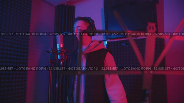 A man rapping through the pop-filter in the microphone - recording his track in the studio - music stand on the foreground. Стоковое видео, видеограф Константин Шишкин / Фотобанк Лори