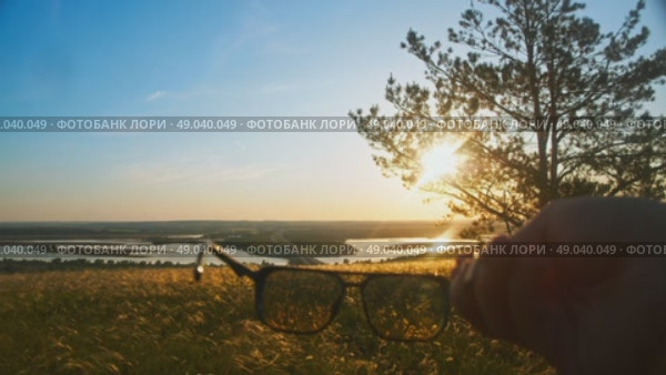 A man takes off his glasses, in awe of the beautiful summer sunset view of nature. Close up. Стоковое видео, видеограф Strunov David / Фотобанк Лори