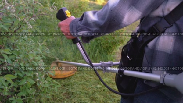 A man with a trimmer mows a garden plot. Стоковое видео, видеограф Igor Skripachev / Фотобанк Лори