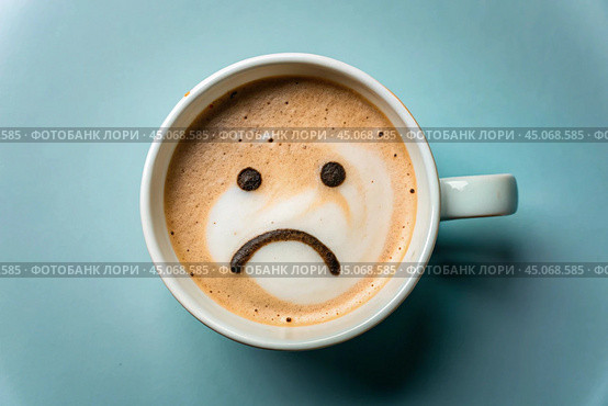 A mug of coffee with a sad smiley face on the foam on the blue table. Top view, flat lay. Стоковое AI-изображение, AI-художник Photojuli / Фотобанк Лори