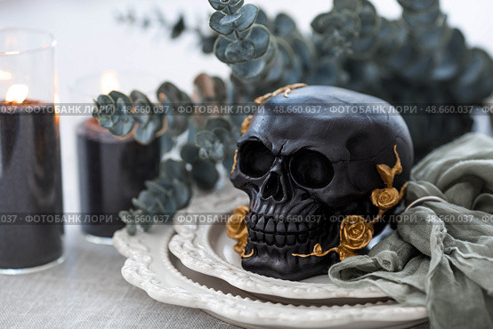 A mysterious black skull with golden roses and pumpkins on serving plates for a Halloween or Day of the Dead party. Стоковое фото, фотограф Photojuli / Фотобанк Лори