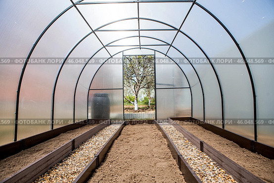 A new greenhouse made of polyethylene and polycarbonate with new beds made of Wood-polymer composite. Preparing for the spring garden season. Installation of a greenhouse in a suburban area. Стоковое фото, фотограф Photojuli / Фотобанк Лори