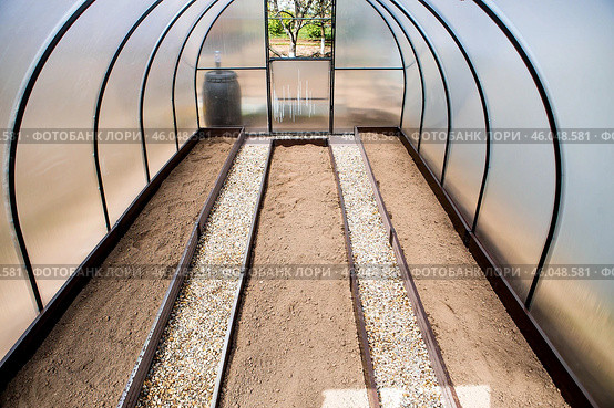 A new greenhouse made of polyethylene and polycarbonate with new beds made of Wood-polymer composite. Preparing for the spring garden season. Installation of a greenhouse in a suburban area. Стоковое фото, фотограф Photojuli / Фотобанк Лори