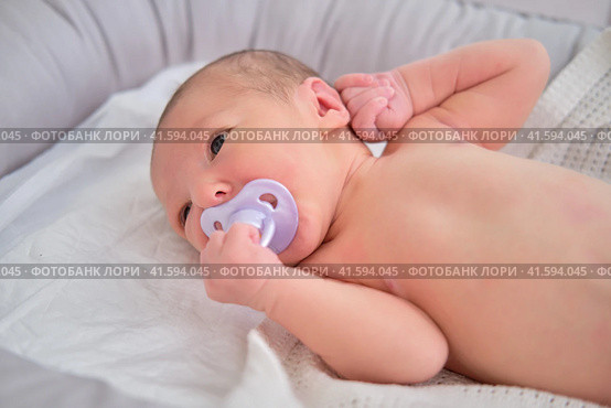 A newborn baby holds a pacifier in his mouth with his hand. Child boy in a cocoon on a crib. Стоковое фото, фотограф Андрей Журавлев / Фотобанк Лори