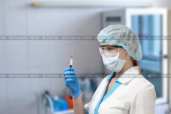 A nurse in a mask and glasses holds a syringe and looks at it, preparing an injection for a patient, Стоковое фото, фотограф Коханова Наталья / Фотобанк Лори