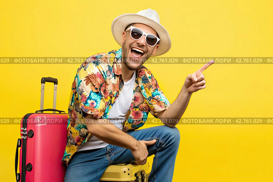 A portrait of a positive man holding a man sitting on a suitcase points with his finger at an empty place highlighted on a yellow background. Стоковое AI-изображение, AI-художник Ярославский Максим / Фотобанк Лори