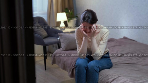 A sad Caucasian woman sits on the couch due to depression in the apartment. Стоковое видео, видеограф Денис Кебедов / Фотобанк Лори