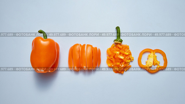 A set of different pieces and a whole ripe orange pepper with a green stem on a gray background. Vegetarian Healthy Food Concept. Top view. Juicy fresh pepper sliced and whole on a gray background. Top view. Стоковое фото, агентство Ingram Publishing / Фотобанк Лори