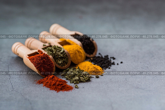 A set of fragrant spices. Turmeric, paprika, herbs and pepper in wooden spoons on a gray background. Free space for text. Стоковое фото, фотограф Photojuli / Фотобанк Лори