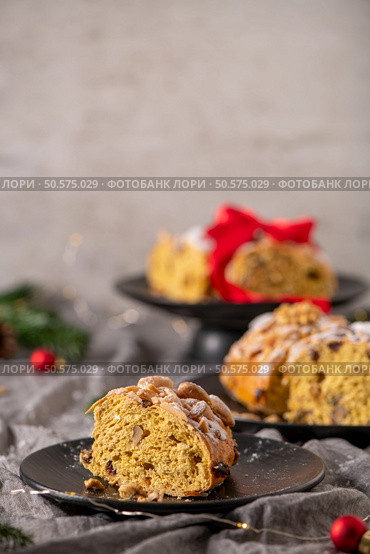 A slice of Bolo Rainha, a Portuguese Christmas cake, is displayed on a black plate with other cakes in the background creating a festive holiday scene. Стоковое фото, агентство Ingram Publishing / Фотобанк Лори