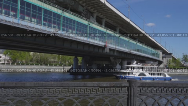 A small steamer passes under the metro bridge while the subway train is moving. It's a sunny day. Russia. Moscow. 01.05.2024. Редакционное видео, видеограф Ярославский Максим / Фотобанк Лори