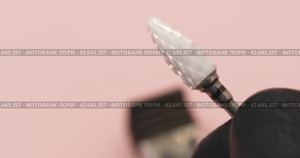 A specialist in gloves holds in his hand a ceramic cutter for hardware manicure with a black notch for removing gel polish with copy space on a pink background. Стоковое видео, видеограф Сергей Чайко / Фотобанк Лори
