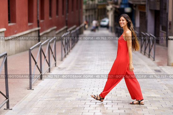 A stylish woman adorned in a vibrant red jumpsuit saunters gracefully along a scenic urban street, effortlessly showcasing her confidence and impeccable fashion sense for all to admire and appreciate. A woman dressed in a striking red jumpsuit is confidently walking down an urban street. Стоковое фото, агентство Ingram Publishing / Фотобанк Лори