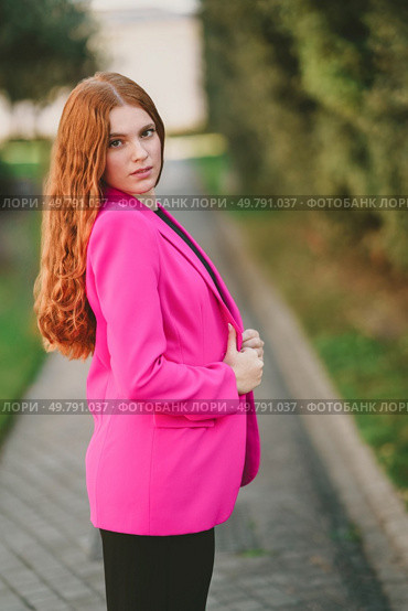 A stylish young woman confidently poses outdoors in a vibrant pink blazer, making a bold statement against a beautifully blurred natural backdrop that enhances her charm and allure. A stylish young woman in a bright pink blazer poses confidently in an outdoor setting. Редакционное фото, агентство Ingram Publishing / Фотобанк Лори