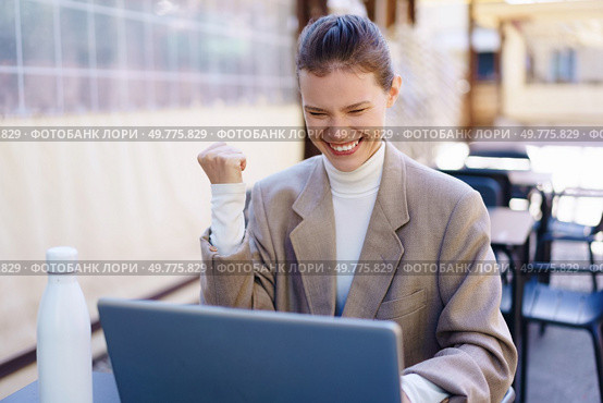 A successful businesswoman in a stylish blazer celebrates her achievement while working on her laptop outdoors, her cheerful expression reflecting professional success and positive energy. Joyful Businesswoman Celebrating Her Success at an Outdoor Workspace with Enthusiasm. Стоковое фото, агентство Ingram Publishing / Фотобанк Лори