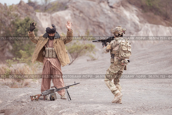 A Taliban soldier stands with a machine gun, Raise hands in surrender to the allied soldiers, In the desert mountain terrain battlefield. Стоковое фото, агентство Ingram Publishing / Фотобанк Лори
