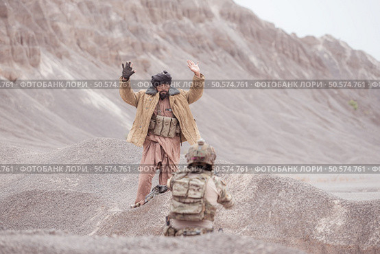 A Taliban soldier stands with a machine gun, Raise hands in surrender to the allied soldiers, In the desert mountain terrain battlefield. Стоковое фото, агентство Ingram Publishing / Фотобанк Лори
