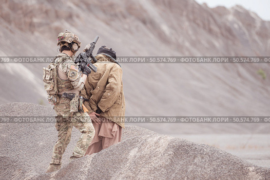 A Taliban soldier stands with a machine gun, Raise hands in surrender to the allied soldiers, In the desert mountain terrain battlefield. Стоковое фото, агентство Ingram Publishing / Фотобанк Лори