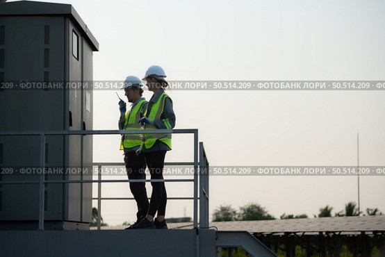 A team of electrical engineers is inspecting an energy storage station of a solar panels in the middle of a hundred acre field of solar panels. Стоковое фото, агентство Ingram Publishing / Фотобанк Лори