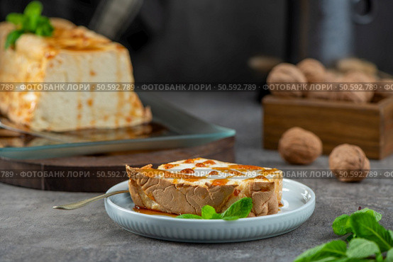 A tempting slice of molotof, a traditional caramelized egg white pudding drizzled with sweet syrup and garnished with fresh mint, is on a light blue plate with the whole pudding nearby. Стоковое фото, агентство Ingram Publishing / Фотобанк Лори