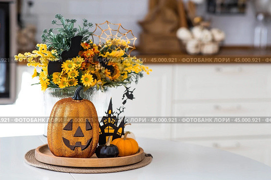 A vase of flowers, pumpkins and a scary castle with a witch on the background of a Scandi-style white kitchen interior. The concept of home and comfort. Autumn decor for Halloween. Стоковое фото, фотограф Photojuli / Фотобанк Лори