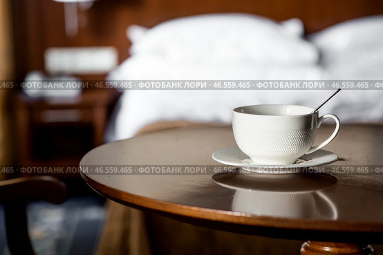 A white cup of hot tea or coffee on a wooden table in the interior of a hotel room. The concept of drinks and comfortable hotel accommodation. Стоковое фото, фотограф Photojuli / Фотобанк Лори