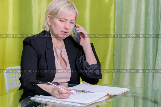 A woman director working in an office is sitting at a table, talking on the phone, checking documents. Стоковое фото, фотограф Юрий Поздников / Фотобанк Лори