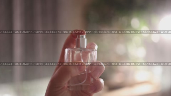 A woman holds a bottle of perfume in her hands and sprays fragrant drops towards the camera. Стоковое видео, видеограф Ольга Коваленко / Фотобанк Лори